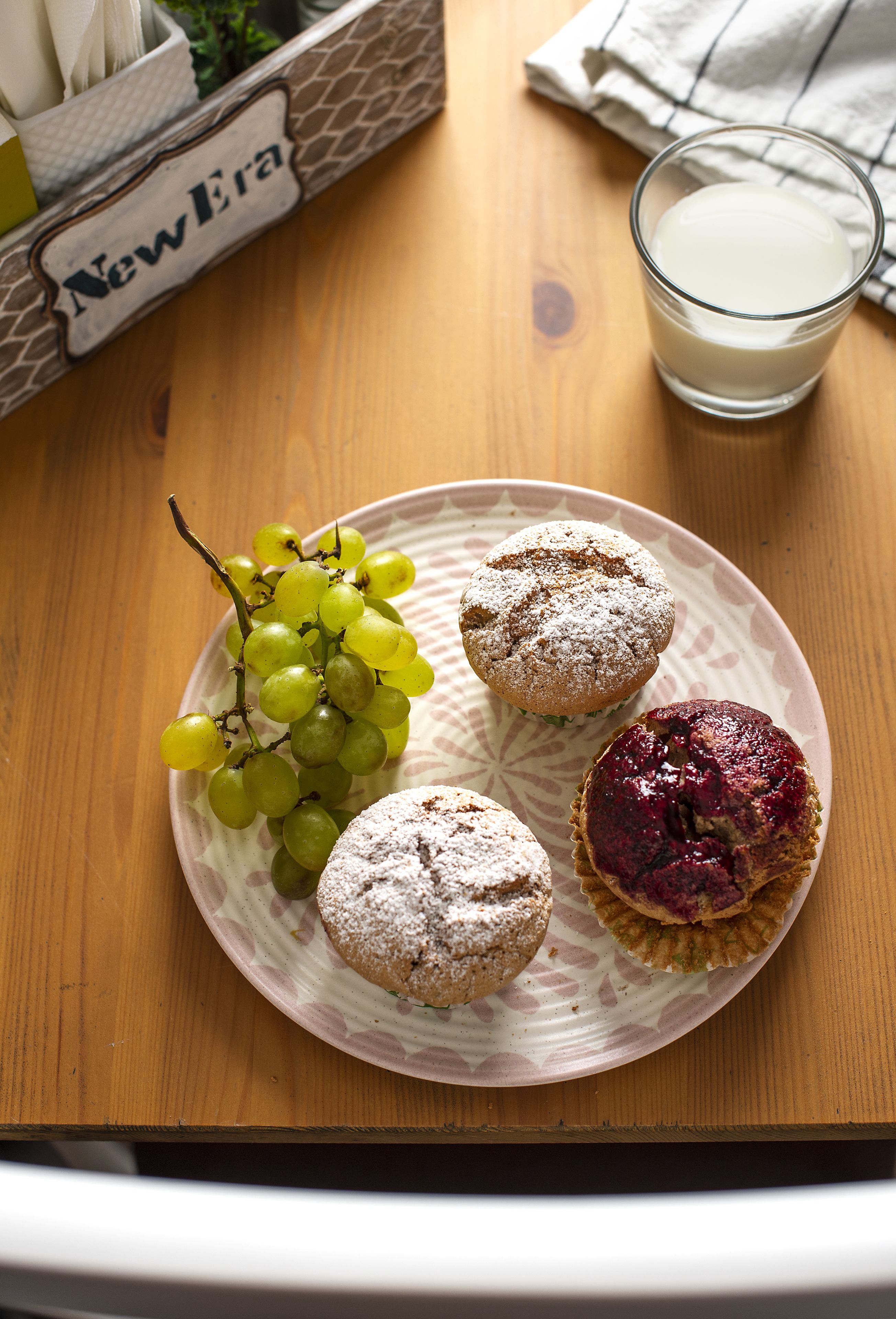Um prato com três muffins e um cacho de uvas sobre uma mesa de madeira.