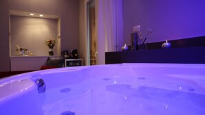 A modern bathroom with a large bathtub, a vanity with a mirror, and a small table with toiletries. - Millina Suites In Navona (Rome)