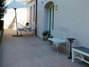 An outdoor patio with a table and chairs, a bench, and a small table with a lamp.