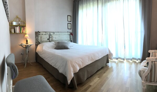 A bedroom with a bed, a bedside table with a lamp, a bookshelf, and a window with curtains.