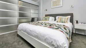 Ein Schlafzimmer mit einem Bett, einem Nachttisch, einer Wandleuchte und einem gerahmten Kunstwerk.
