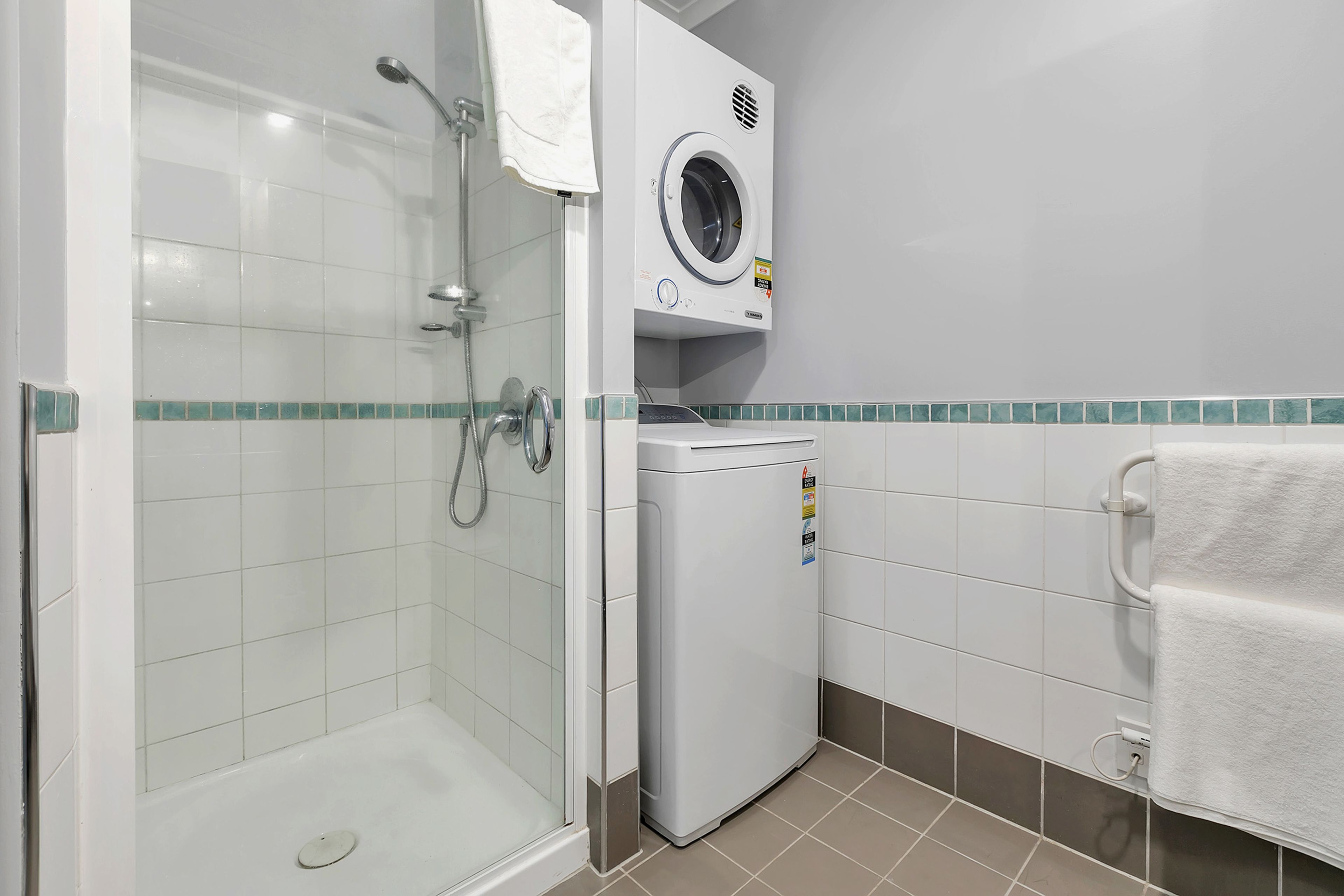 A bathroom with a glass-enclosed shower, a built-in washing machine, and a towel rack.