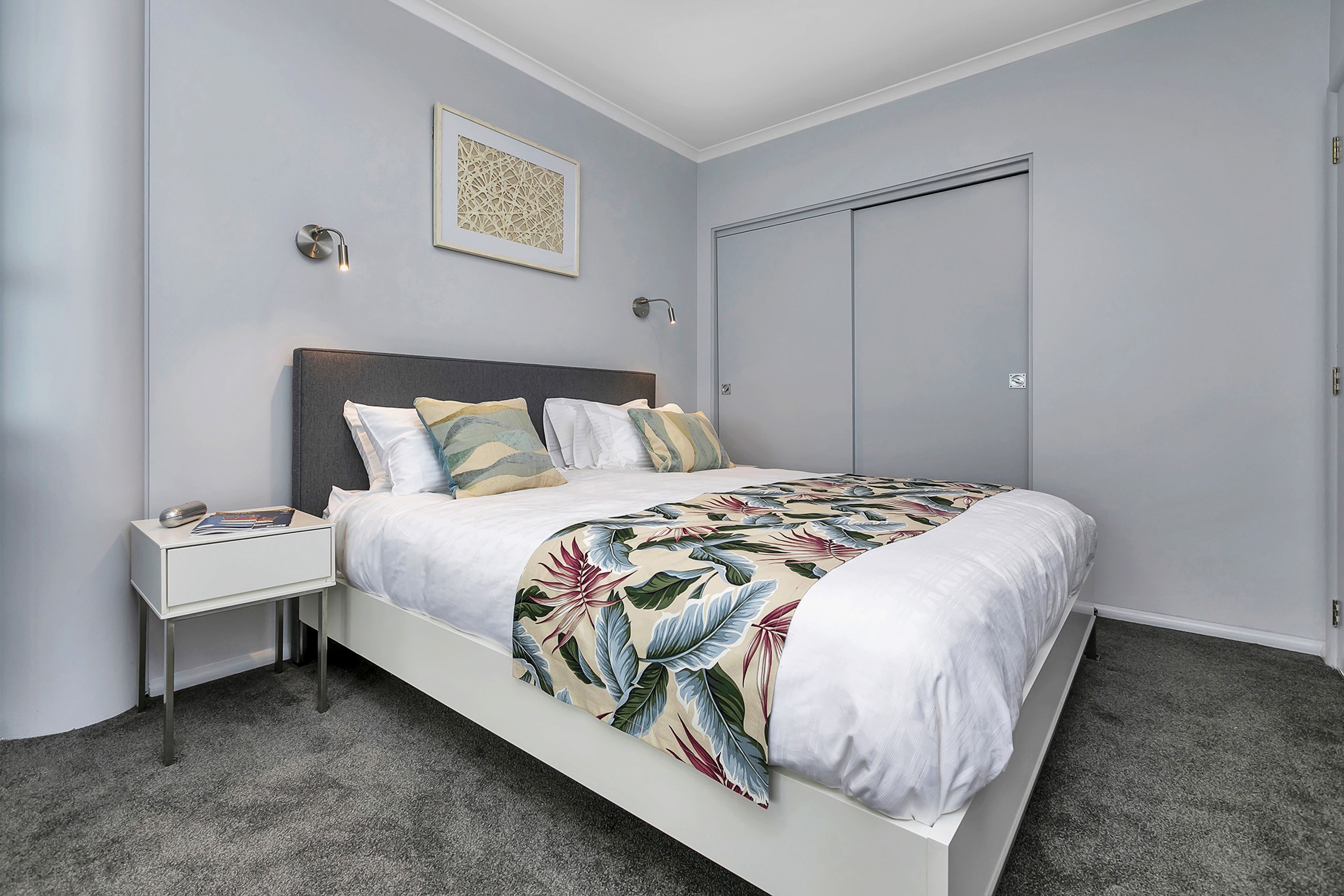 Een slaapkamer met een bed, nachtkastje en een deur.