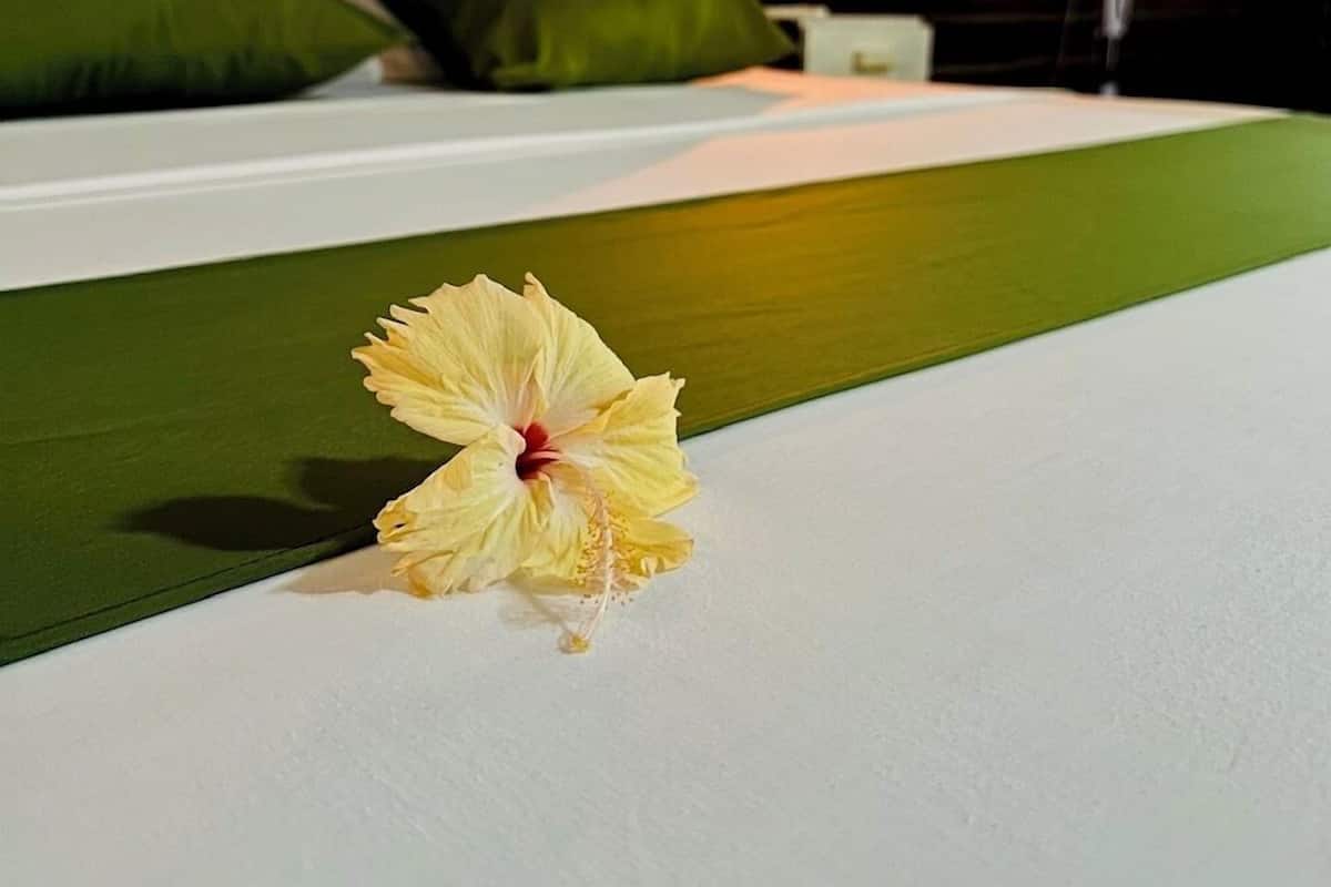 A bed with green bedding and a single yellow hibiscus flower.