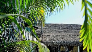 Un espacio de estar al aire libre con techo de paja, mesa y sillas de madera, rodeado de abundante vegetación.