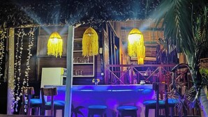 Un área de bar al aire libre con muebles de madera y luces amarillas colgantes.