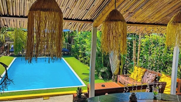 Un área de piscina con techo de paja, una silla de descanso y una mesa con un florero y una botella.