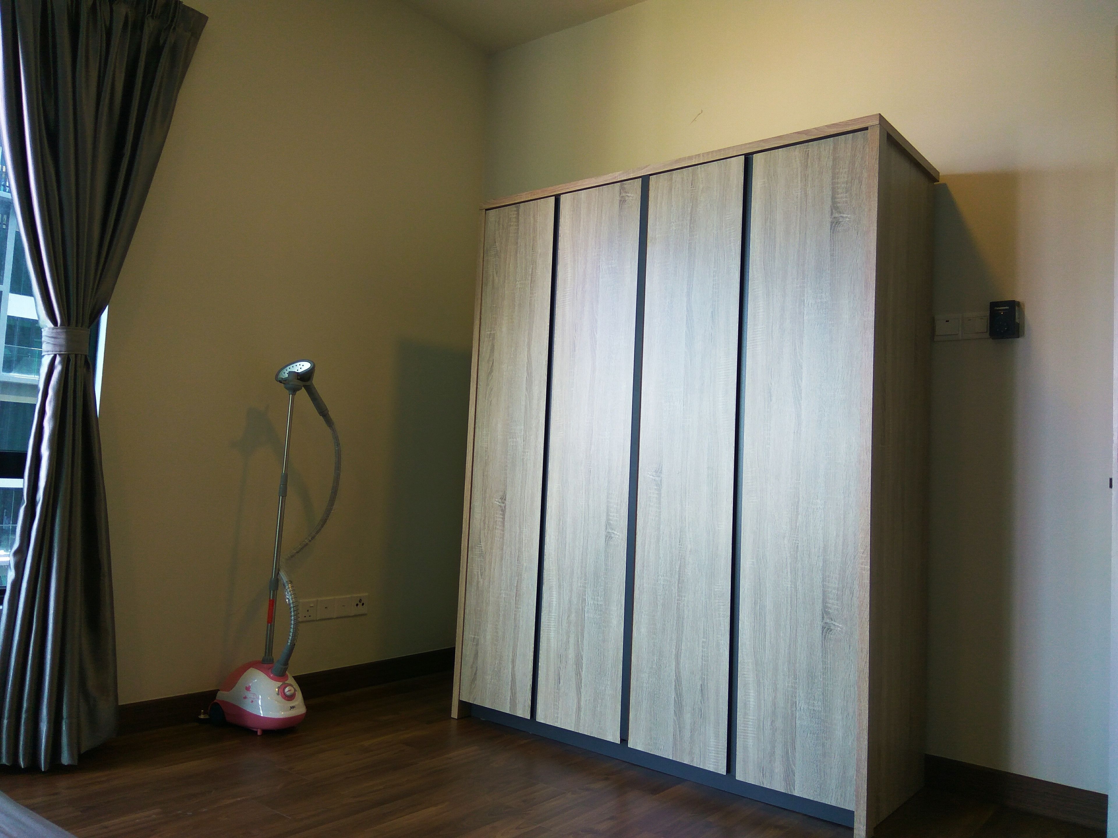 Una habitación con un armario de madera, un aspirador y una ventana con cortinas.