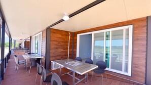 A modern outdoor dining area with a long table and chairs, large windows, and a wooden deck. - Golden Field Pension (Yeosu)