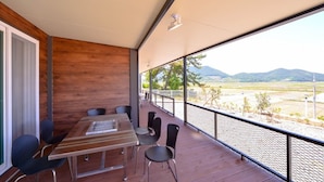 A balcony with a wooden table and chairs, a view of a landscape with mountains and trees. - Golden Field Pension (Yeosu)