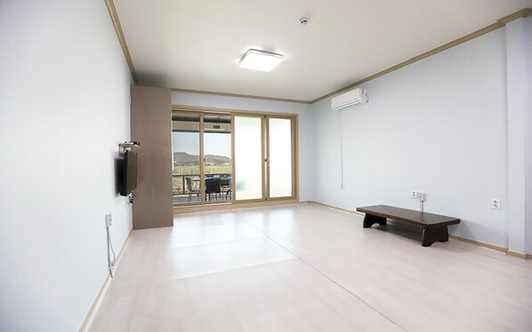 A spacious room with a large sliding glass door leading to an outdoor area, a flat-screen TV mounted on the wall, and a bench in the center.