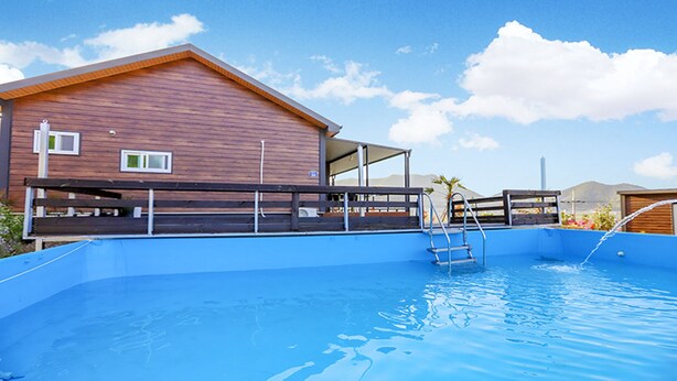 A swimming pool with a wooden deck and a building in the background. - Golden Field Pension (Yeosu)