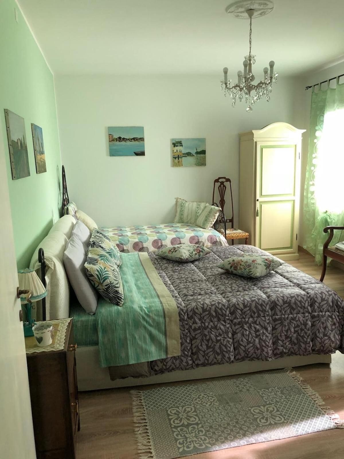 A bedroom with a bed, a dresser, a chandelier, and artwork on the walls.