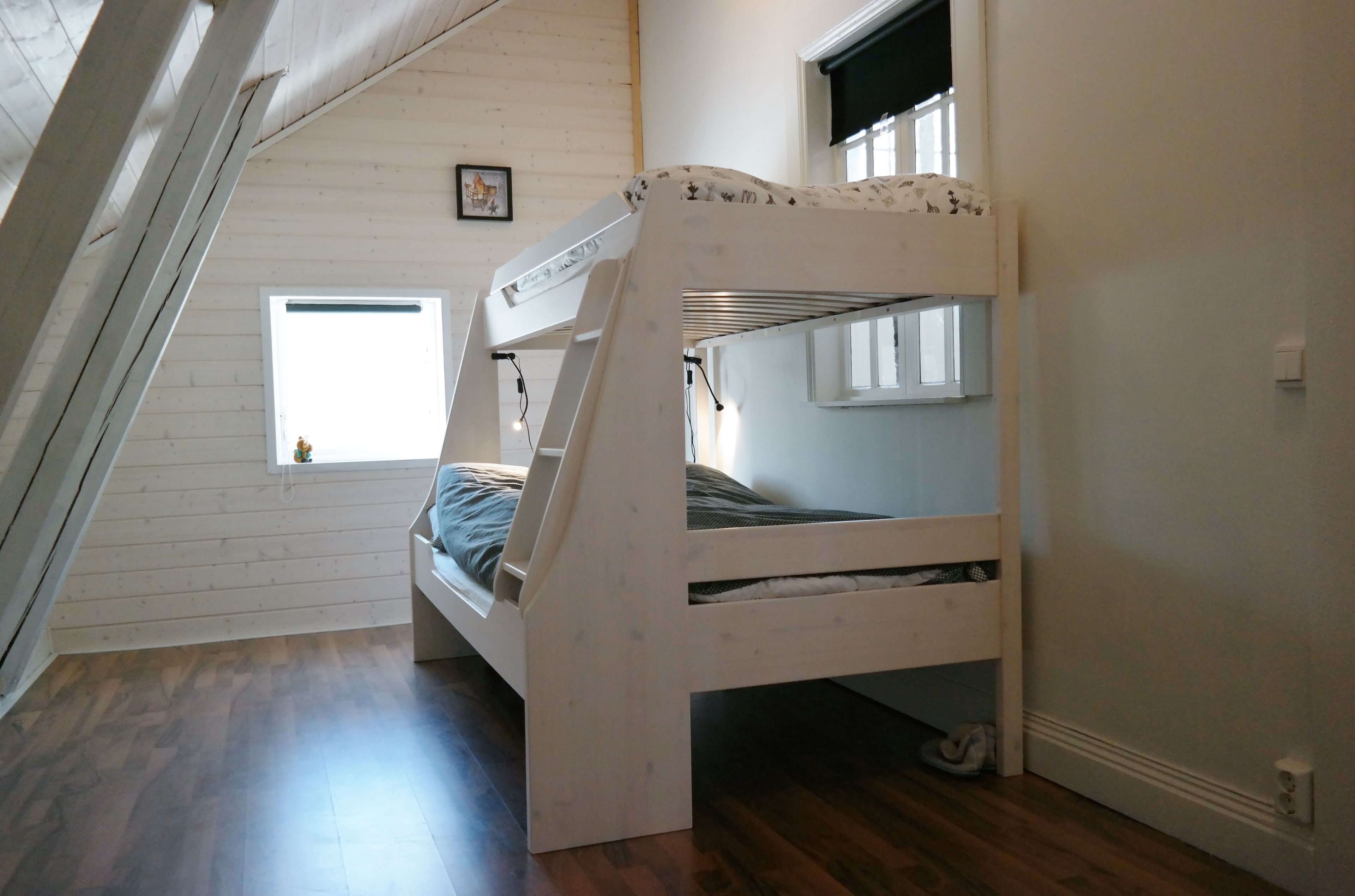 A bunk bed in a room with wooden walls, a small window, and a visible electrical outlet.