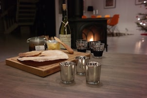 Una mesa de madera con un pan, una botella de vino, un frasco de mermelada y copas para chupitos.