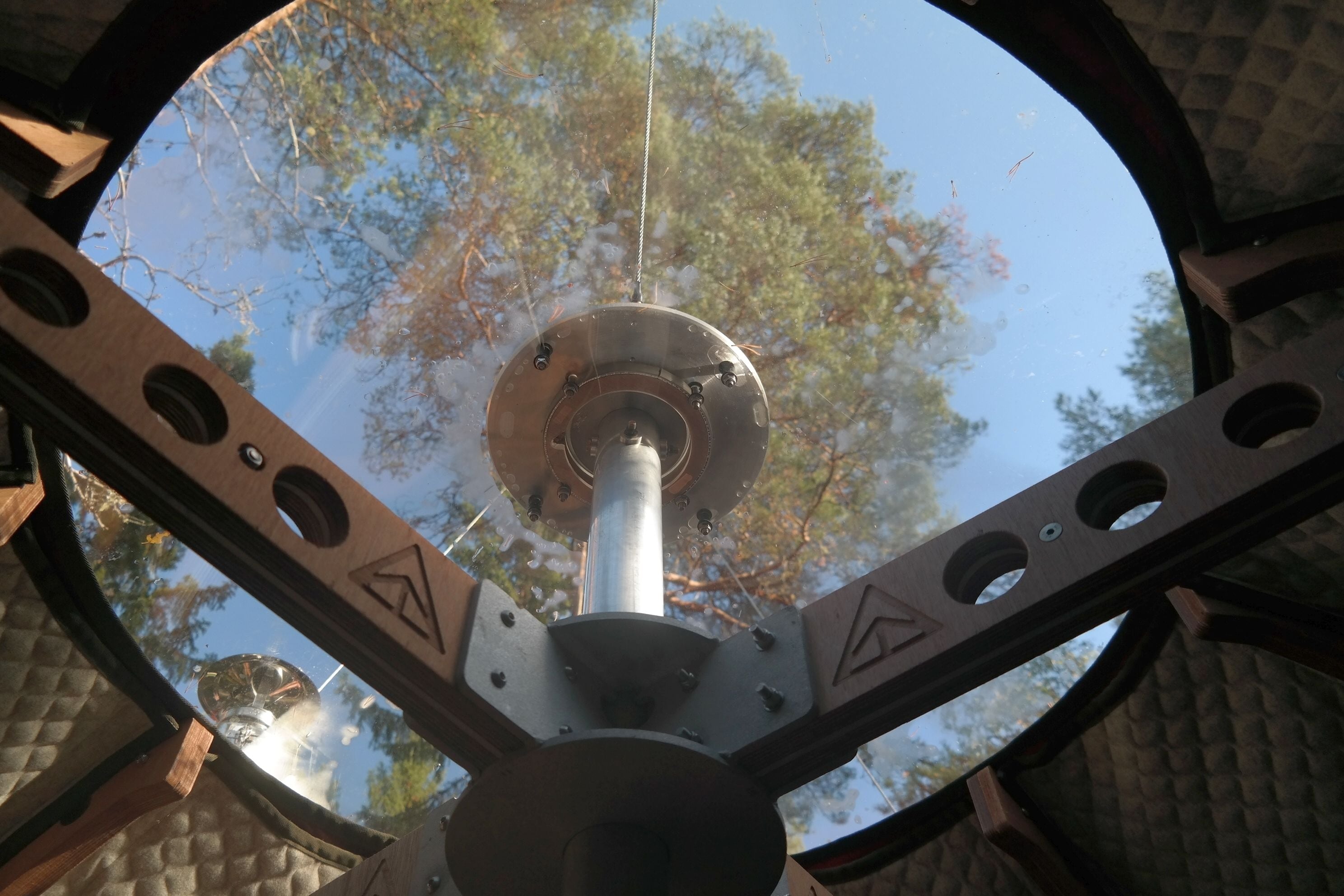 A view through a telescope's lens, focusing on a metal structure with circular cutouts and a central hub.