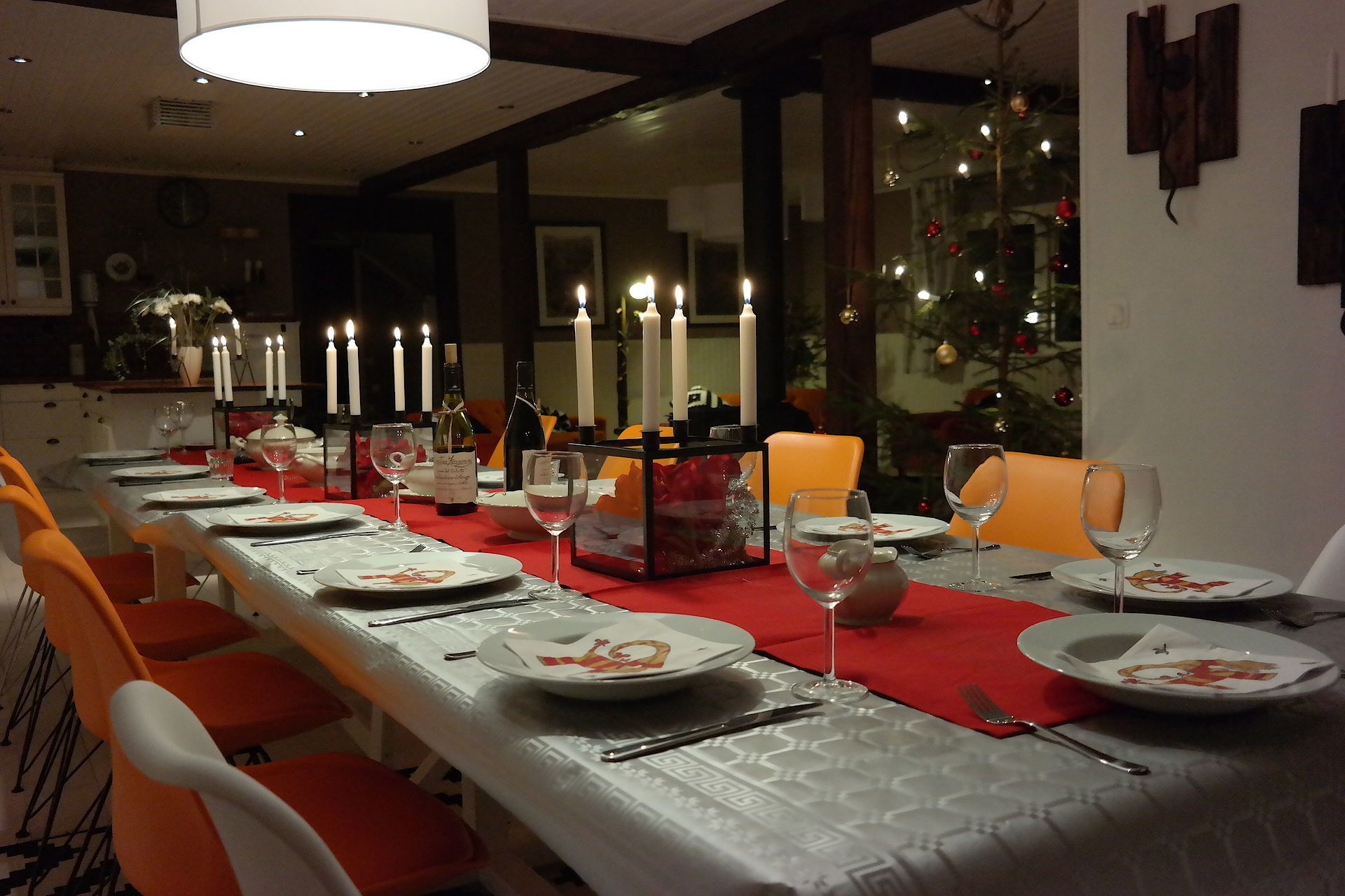 Een eetgedeelte met een lange tafel gedekt voor een maaltijd, kaarsen en een kerstboom op de achtergrond.