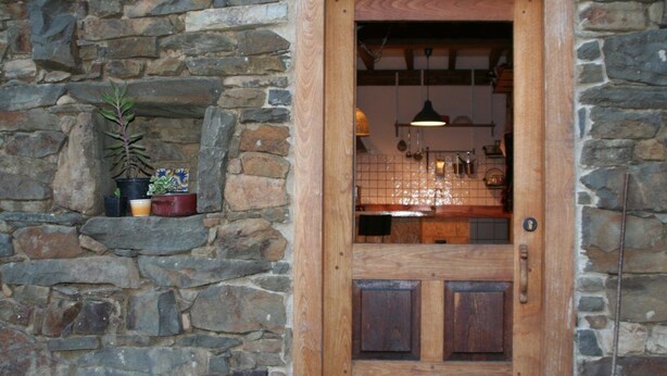Une porte en bois, un mur en pierre, une plante en pot et un luminaire suspendu.