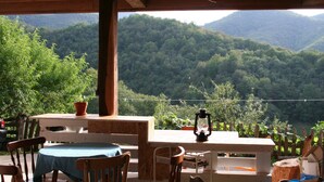 Une table et des chaises en bois sont disposées à l’extérieur, offrant une vue sur une chaîne de montagnes boisées.