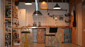 Une cuisine dotée d’un plan de travail en marbre, de deux tabourets de bar, de casseroles suspendues et d’une étagère en bois où sont rangés des bocaux.