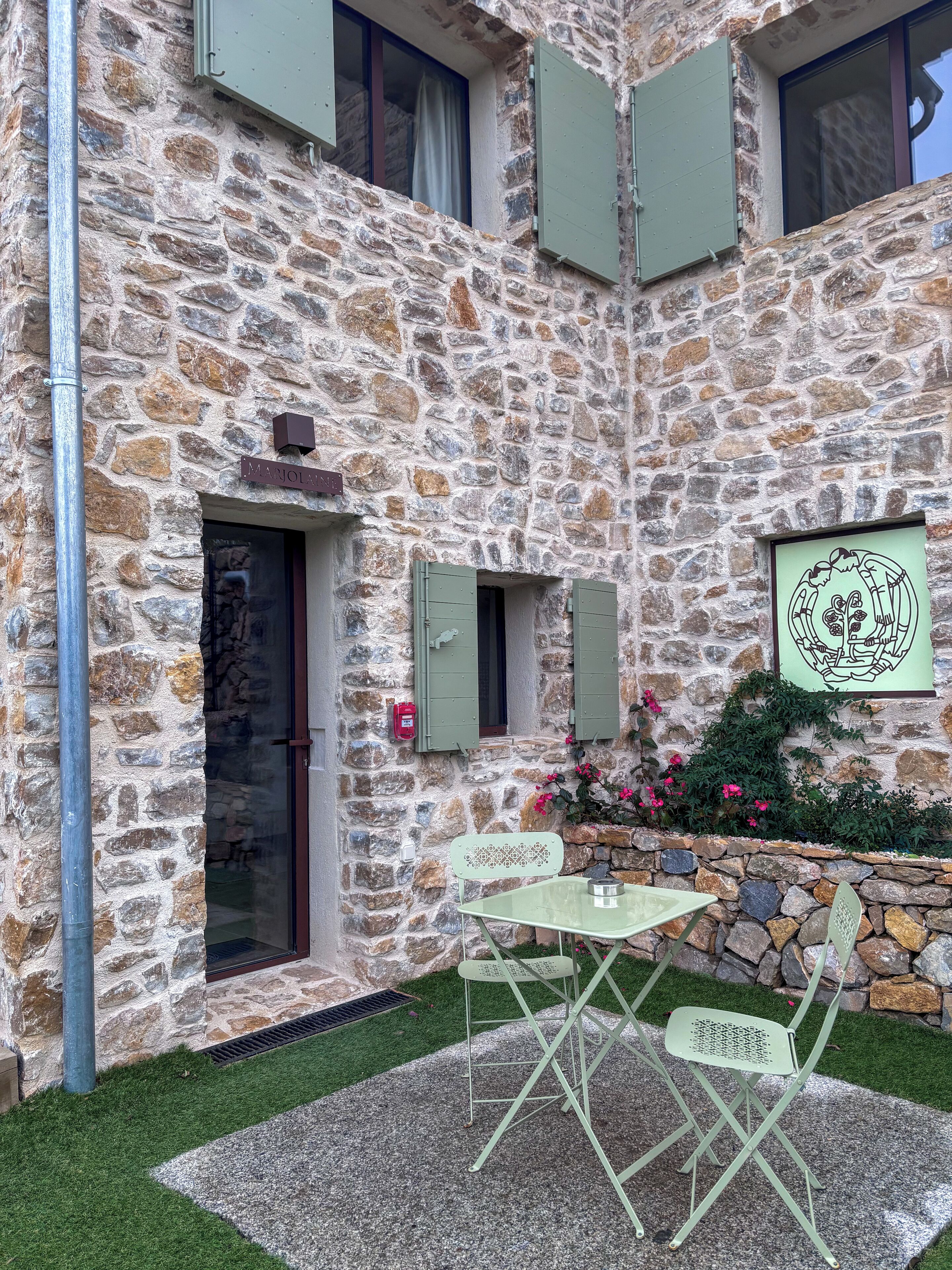 A stone building with a door, windows, and a small table with chairs in the courtyard.