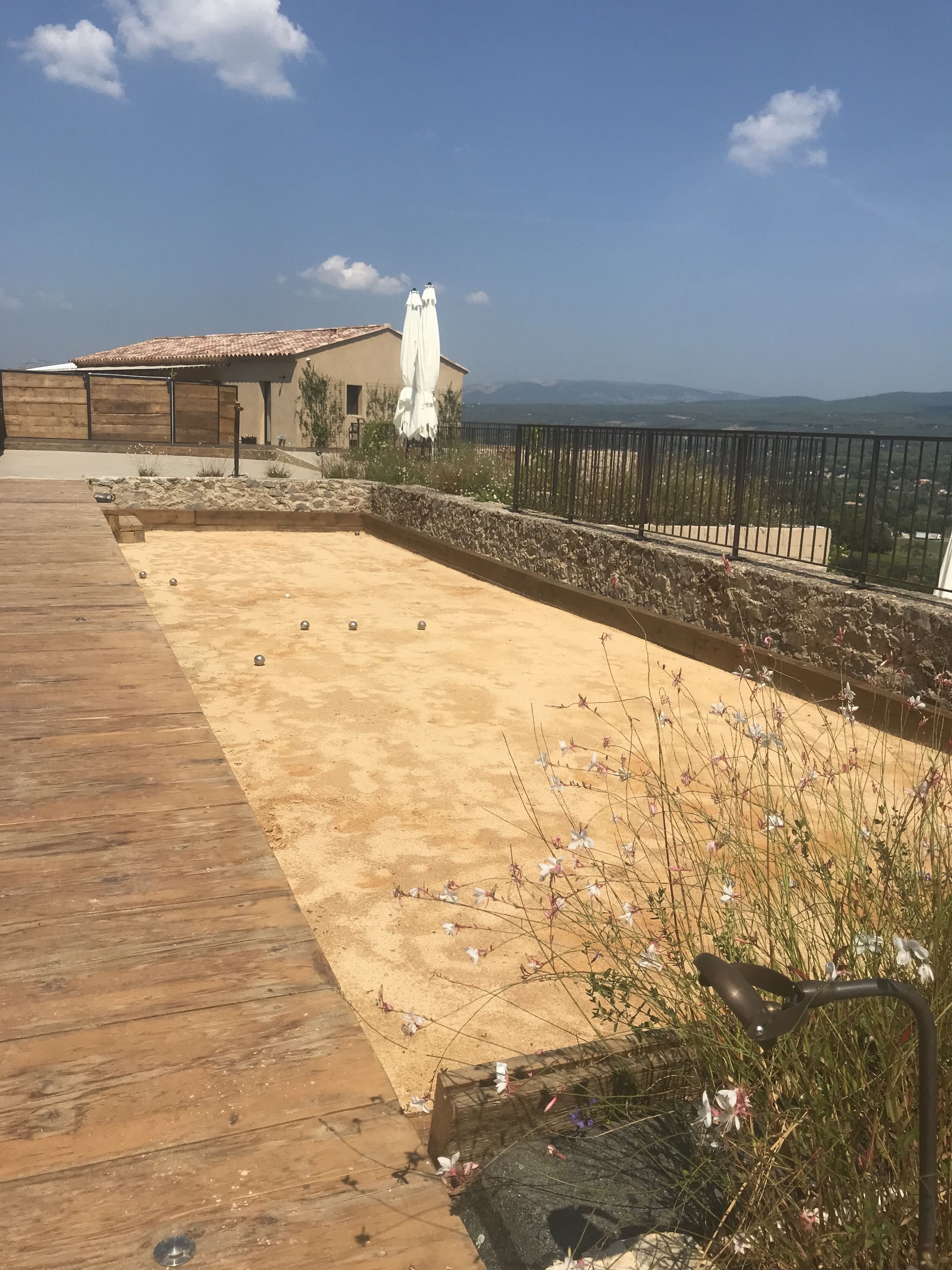 Una terraza de madera con zona arenosa, pared de piedra y vistas a las montañas.