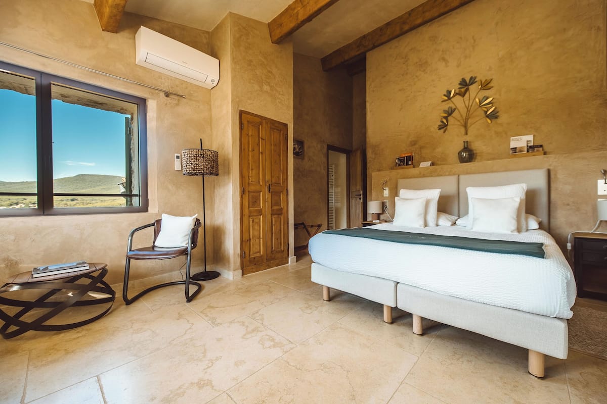 Un dormitorio con una cama grande, una silla, una mesita y una ventana con vistas al desierto.