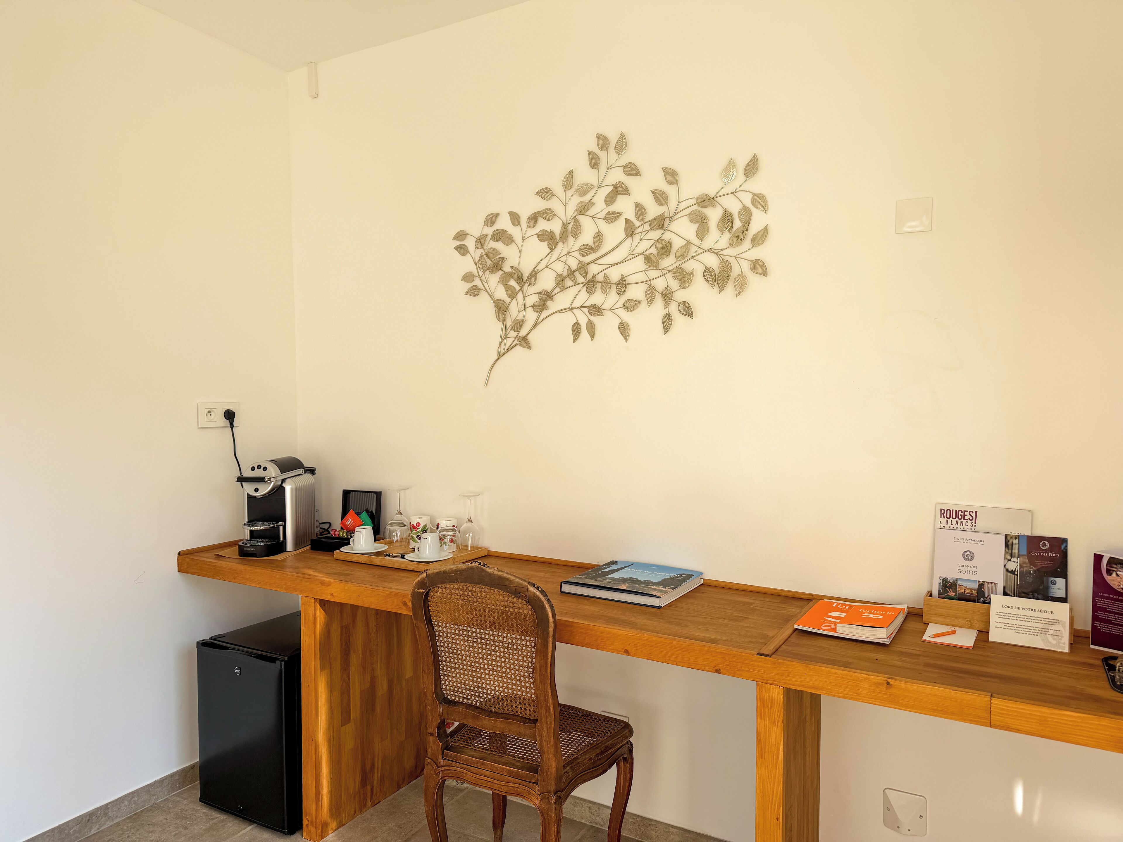 A small office with a wooden desk, a chair, a coffee machine, and a wall decoration.
