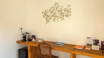 A small office with a wooden desk, a chair, a coffee machine, and a wall decoration.