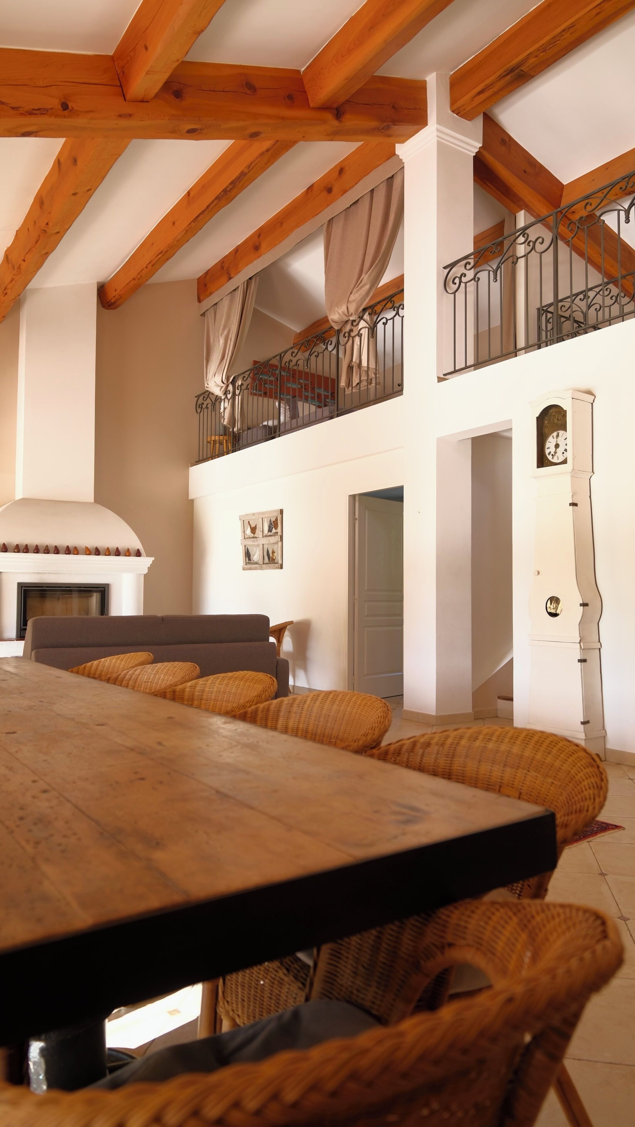 Un salón amplio con una gran mesa de madera, sillas de mimbre, una chimenea y una escalera con barandilla de hierro forjado.