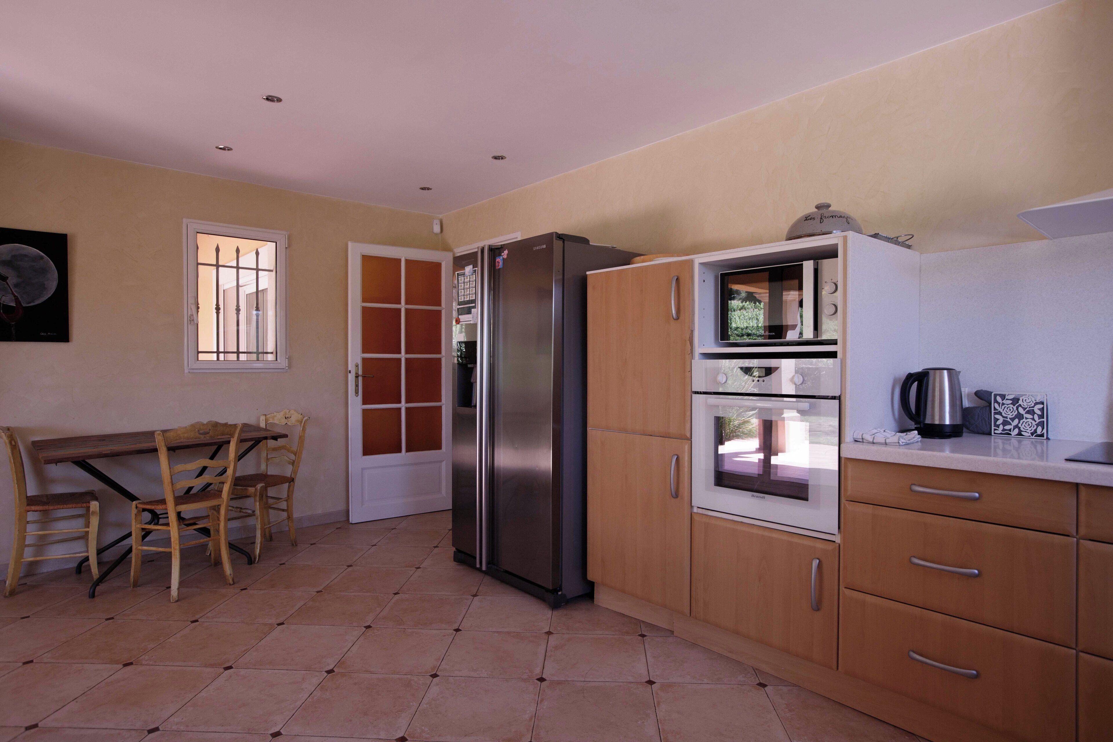 A kitchen with a refrigerator, oven, and a dining table with chairs.