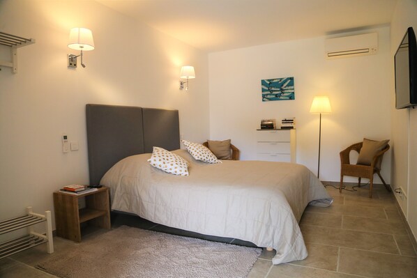 Een slaapkamer met een groot bed, nachtkastjes, een staande lamp, een stoel en een aan de muur bevestigde televisie.