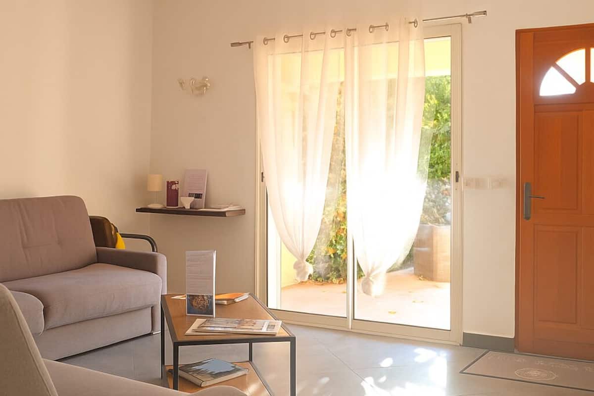 Una sala de estar con sofá, una mesa de centro y un ventanal corredizo que da a un espacio exterior.
