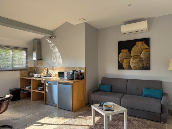 Un espacio habitable funcional con kitchenette, un sofá gris y una pequeña mesa de centro.