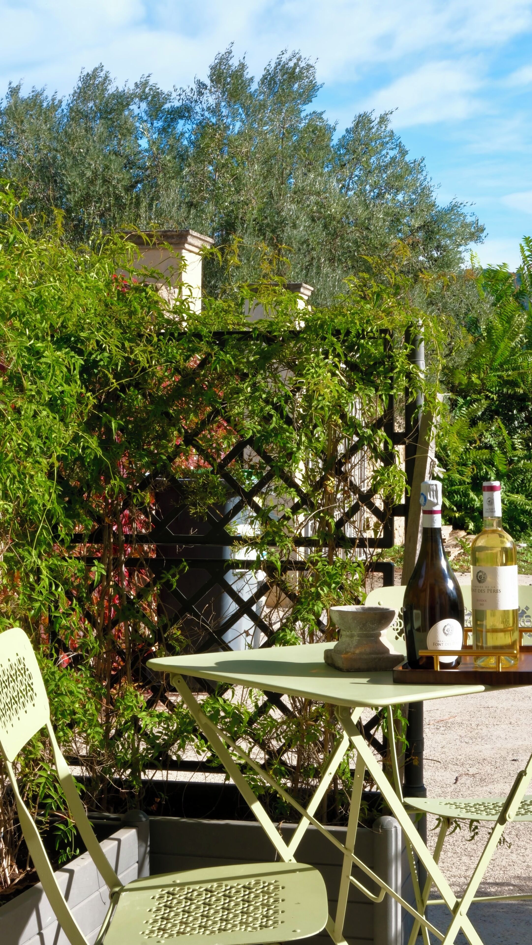 En udendørs terrasse med et bord, stole og vinflasker.