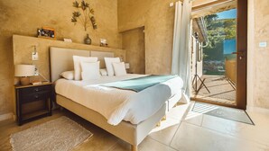 Een slaapkamer met een groot bed, een nachtkastje, een lamp en uitzicht op het buiten via een deur.