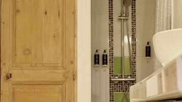 Puerta de madera que da a un baño con ducha, lavabo y artículos de aseo en las repisas.