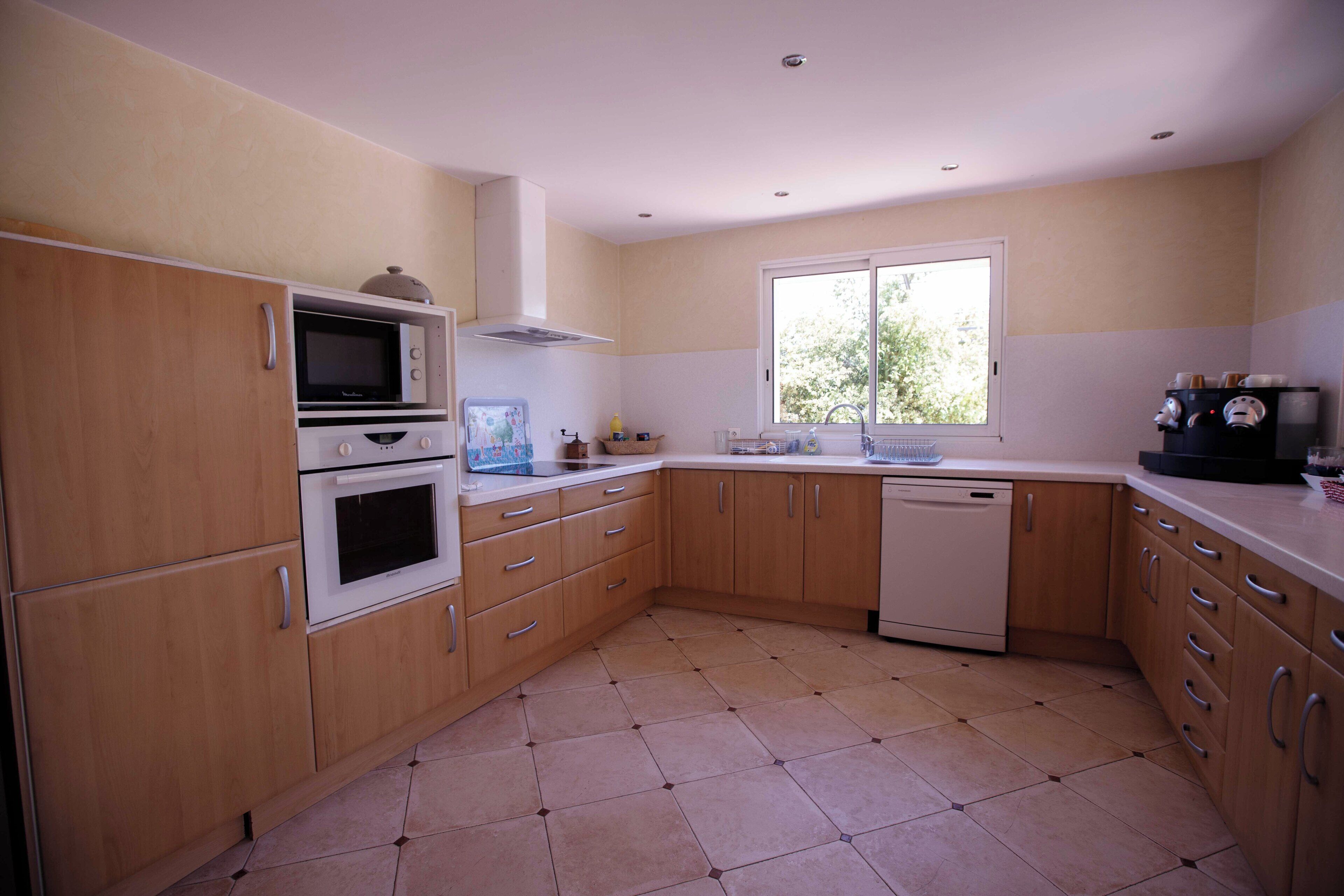 A kitchen with wooden cabinets, a microwave, an oven, a dishwasher, and a window providing natural light.