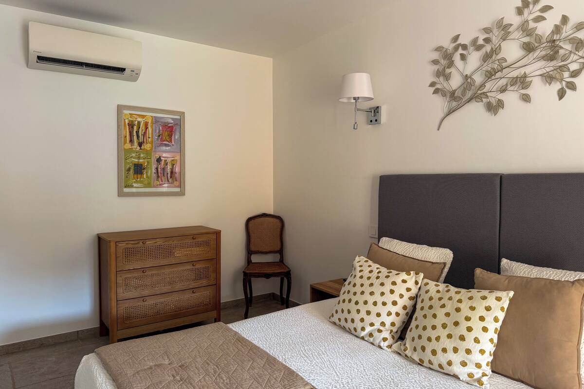 Un dormitorio con cama, cómoda, silla, lámpara de pared y un adorno en la pared.