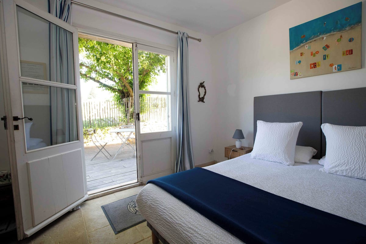 Un dormitorio con cama, mesita de noche, un cuadro y puerta corrediza de vidrio que da a un espacio exterior.