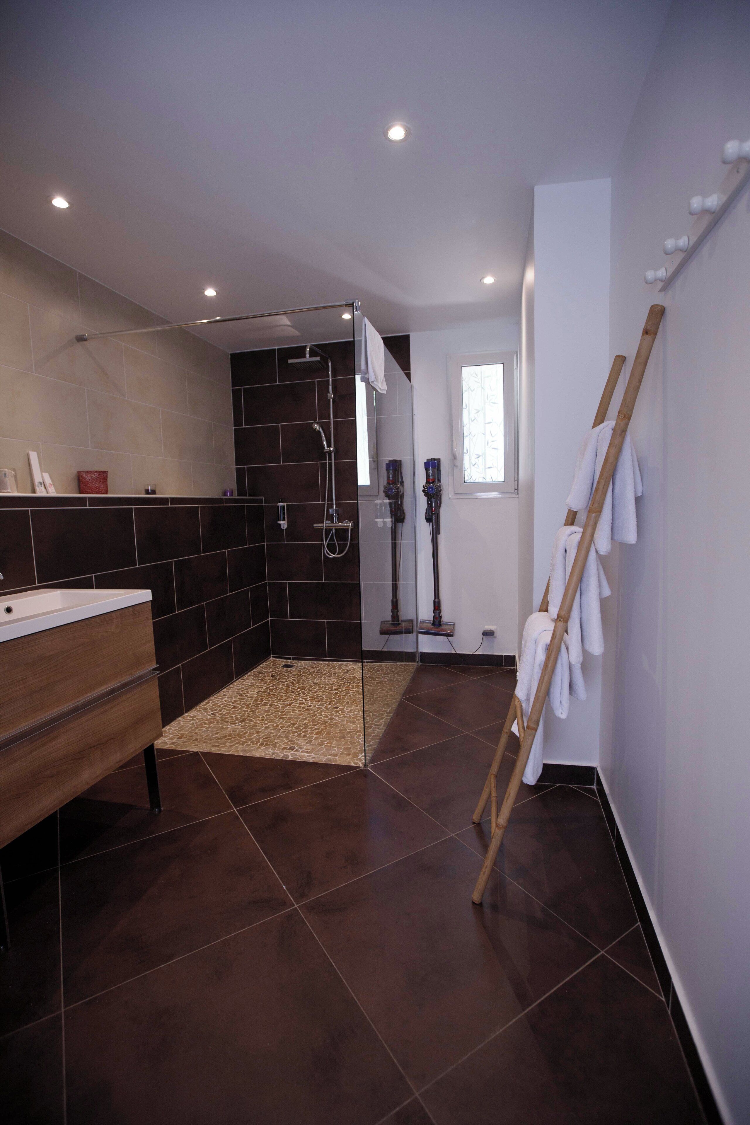A modern bathroom with a shower, a wooden bench, and a towel rack.