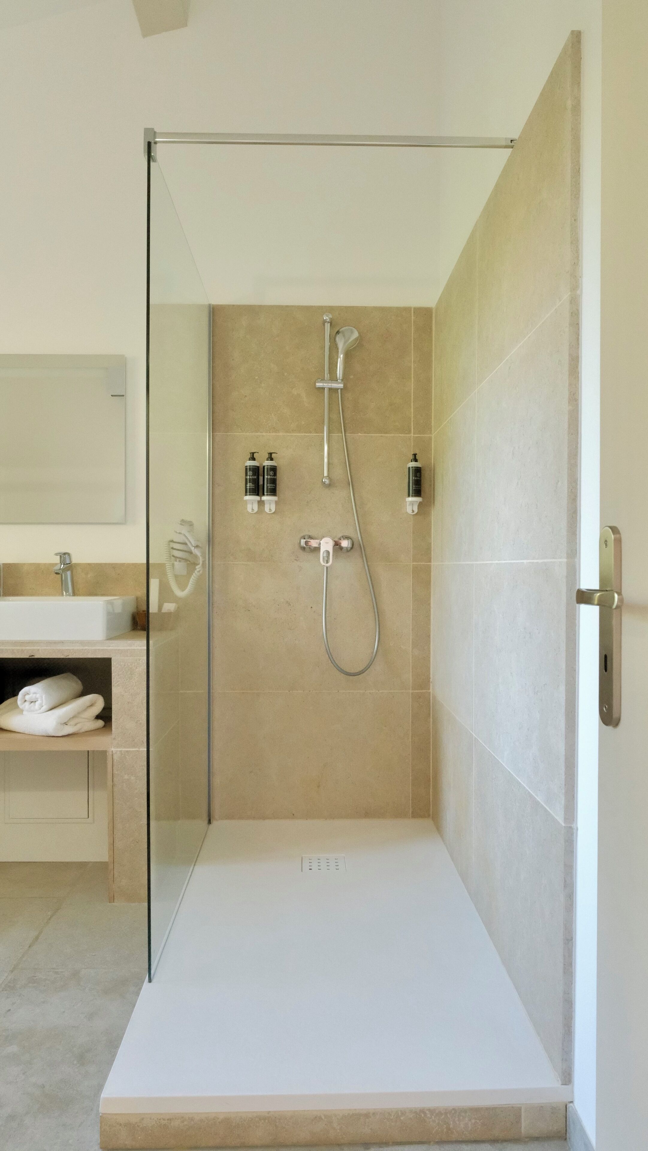 Een moderne badkamer met een douchecabine van glas, een wit wastafelmeubel en beige tegels.