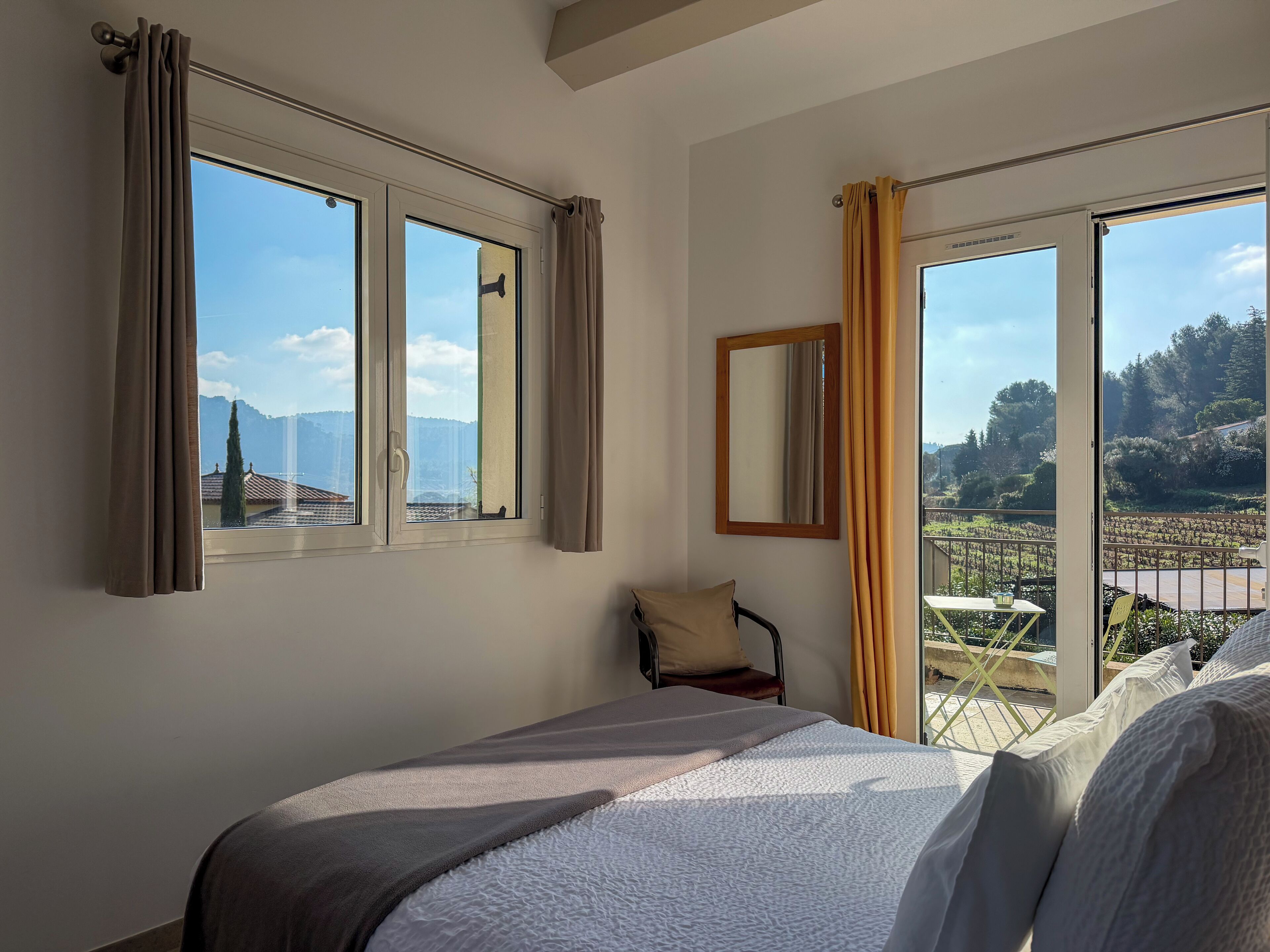 Ein Hotelzimmer mit einem großen Bett, einem Sessel, einem Fenster mit Vorhängen und einem Balkon mit Bergblick.
