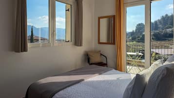 Ein Hotelzimmer mit einem großen Bett, einem Sessel, einem Fenster mit Vorhängen und einem Balkon mit Bergblick.
