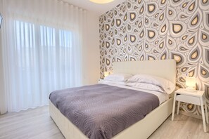 A modern bedroom with a bed, white nightstands, and a patterned wallpaper. - Flower Suites Sorrento (Sorrento)