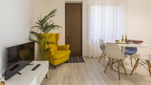 Una sala de estar moderna con televisor de pantalla plana, un sillón amarillo, una mesa de comedor con sillas y una planta en maceta.