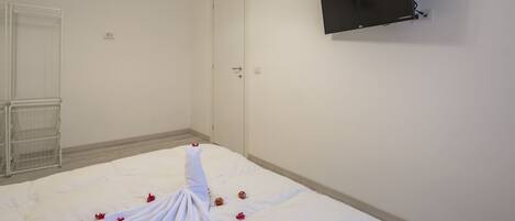 A hotel room with a bed, a TV mounted on the wall, and a door.
