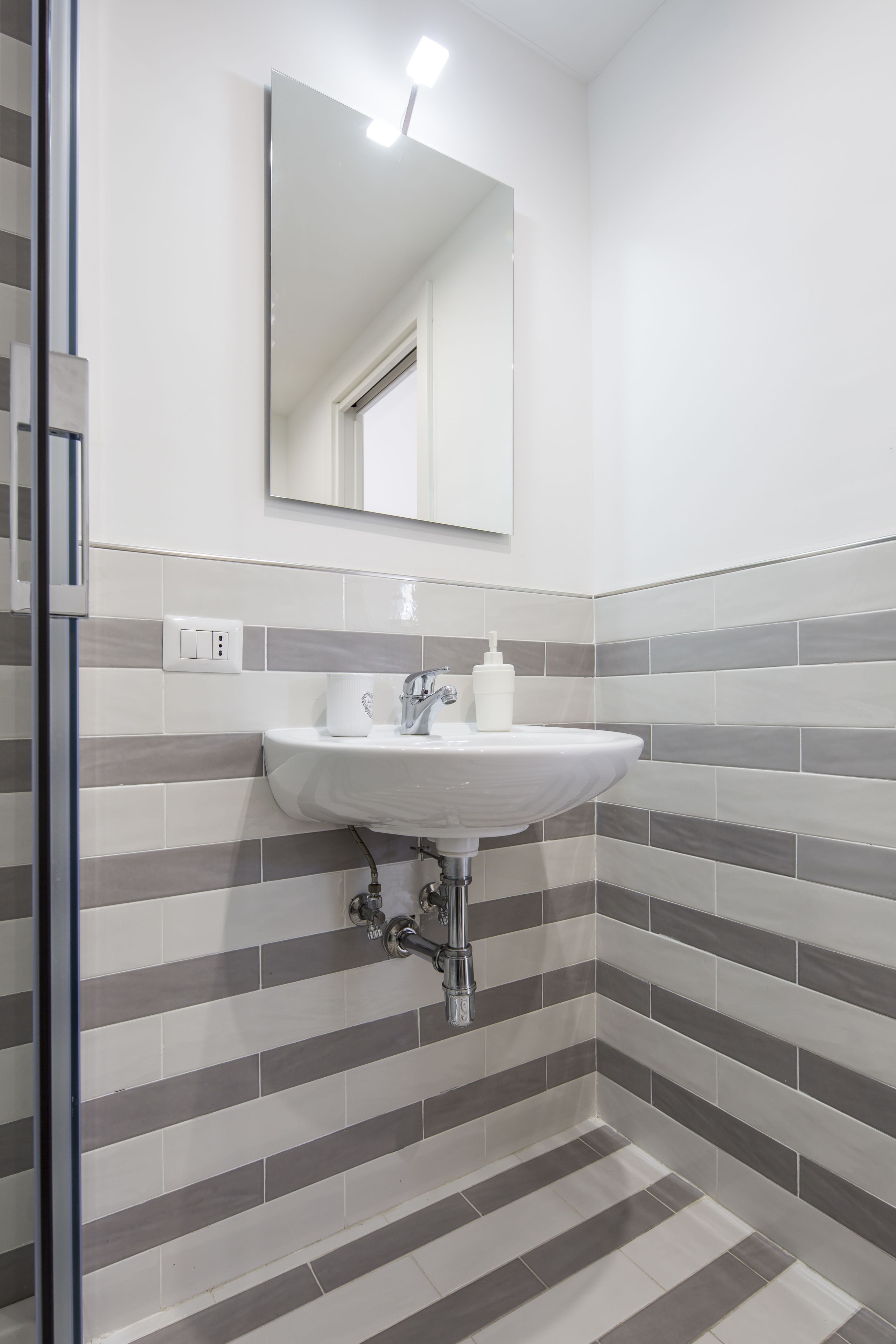 Un bany amb un lavabo blanc, un mirall damunt i parets de rajola a ratlles.