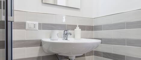 Un bany amb un lavabo blanc, un mirall damunt i parets de rajola a ratlles.