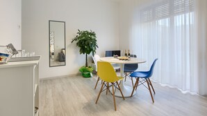 Un comedor moderno con una mesa redonda, sillas amarillas y azules, una planta en maceta y un espejo grande en la pared.